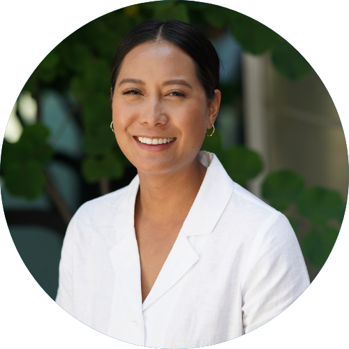 woman in white shirt smiling in front of green foliage