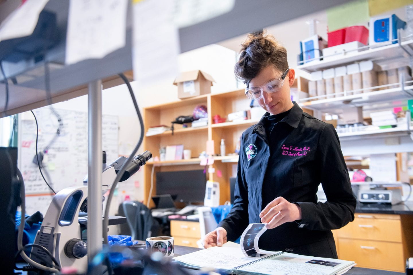 A researcher wearing safety goggles studies a notebook in a lab