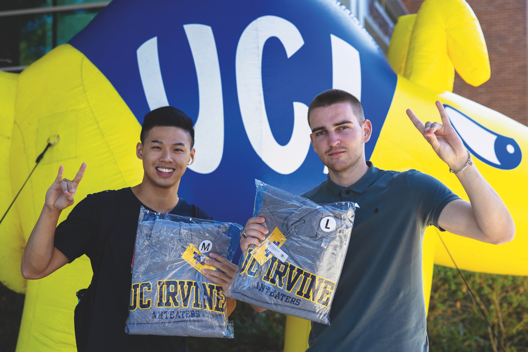 Two Anteaters holding up sweatshirts and flashing the UCI sign