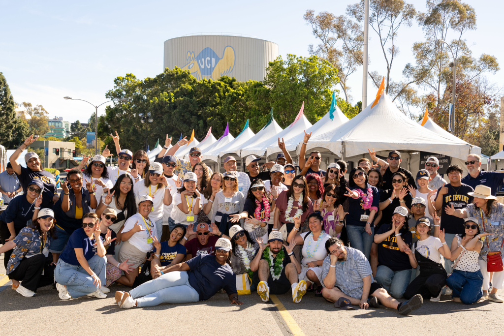 A large group of alumni and community members pose for a group photo outdoors at a UCI event.