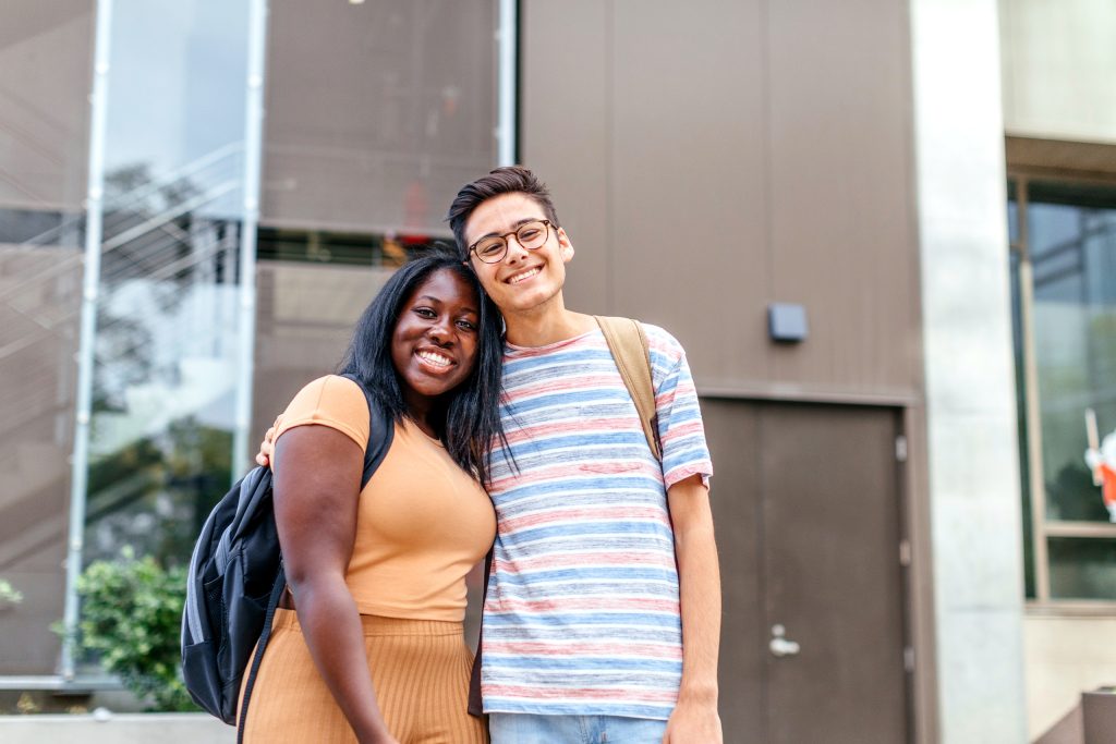 Two students with backpacks stand together outside a campus building.