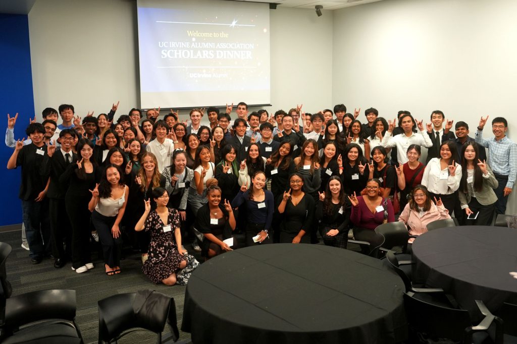 Large group of students pose at a UC Irvine Alumni Association Scholars Dinner event in front of a presentation screen.