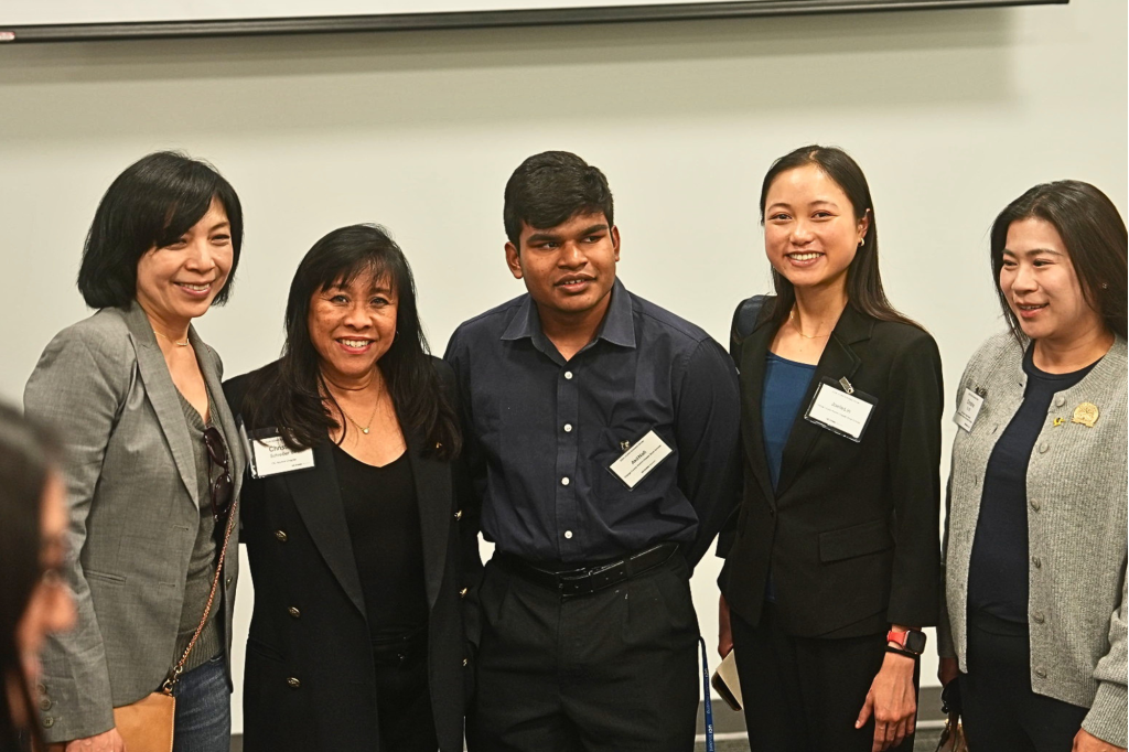 Five attendees at the UC Irvine Alumni Association Scholars Dinner pose together in a conference room, wearing name badges with a presentation screen behind them.