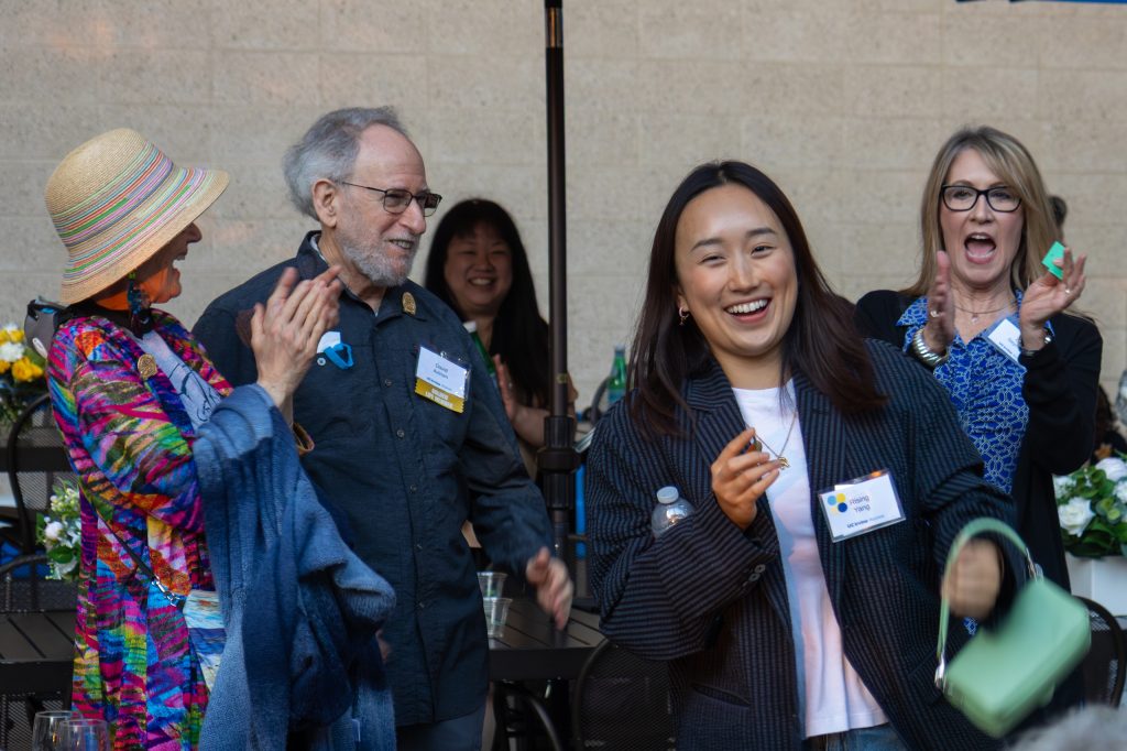 A diverse group of people clapping and smiling, celebrating together at an event.