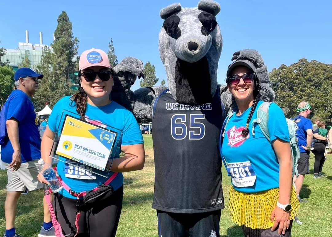 Two people with race numbers on their shirts pose with an Anteater mascot