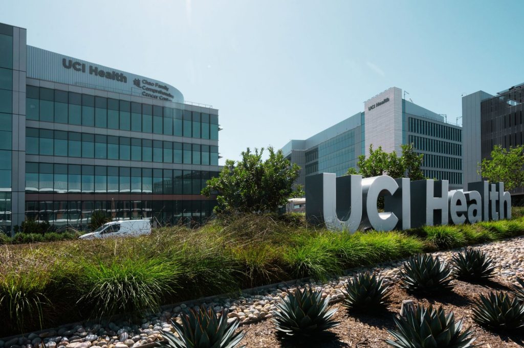 Three hospital buildings built closely together with a metal sign in front that says "UCI Health"