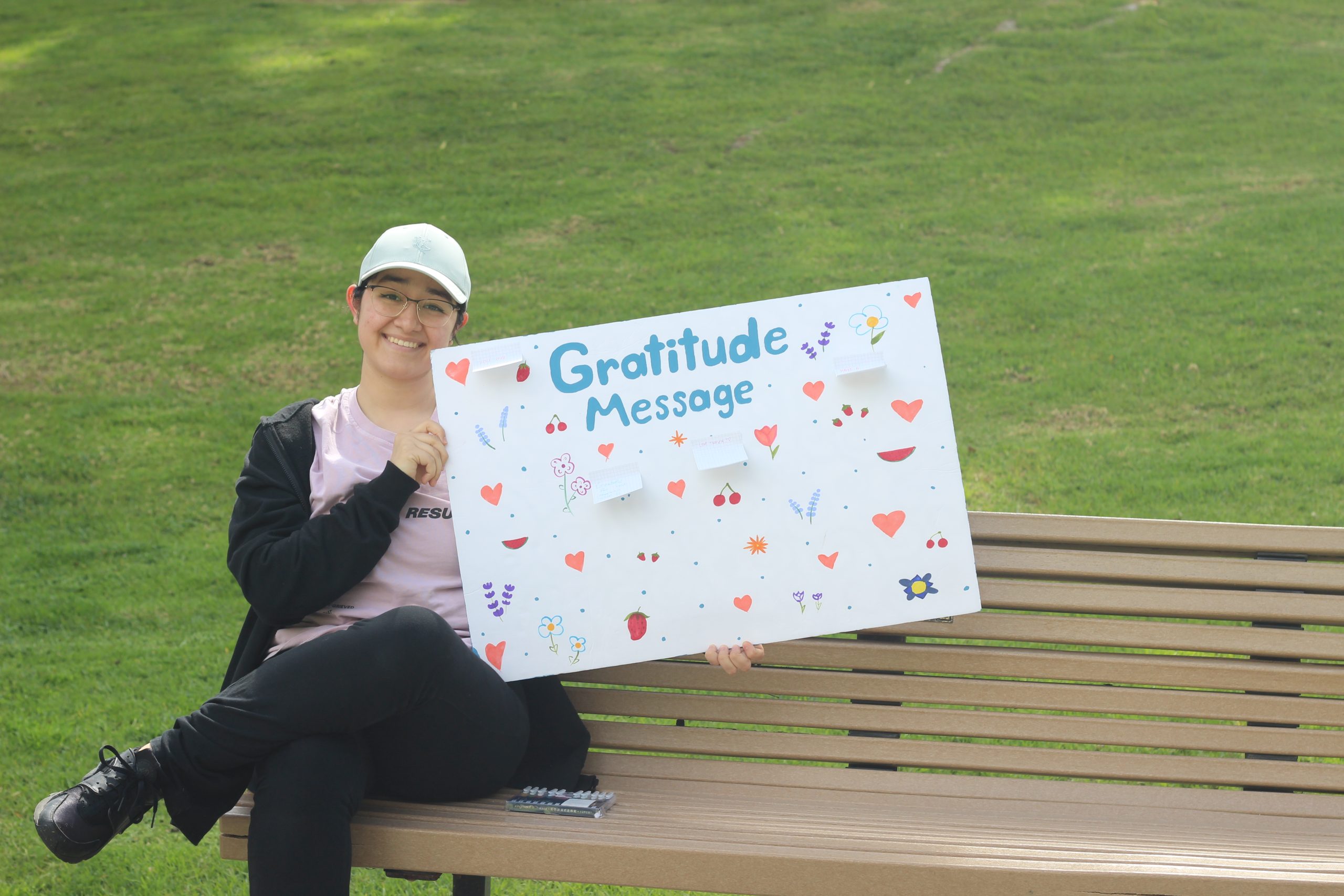 A student sits on a bench and holds a sign that says "Gratitude message"