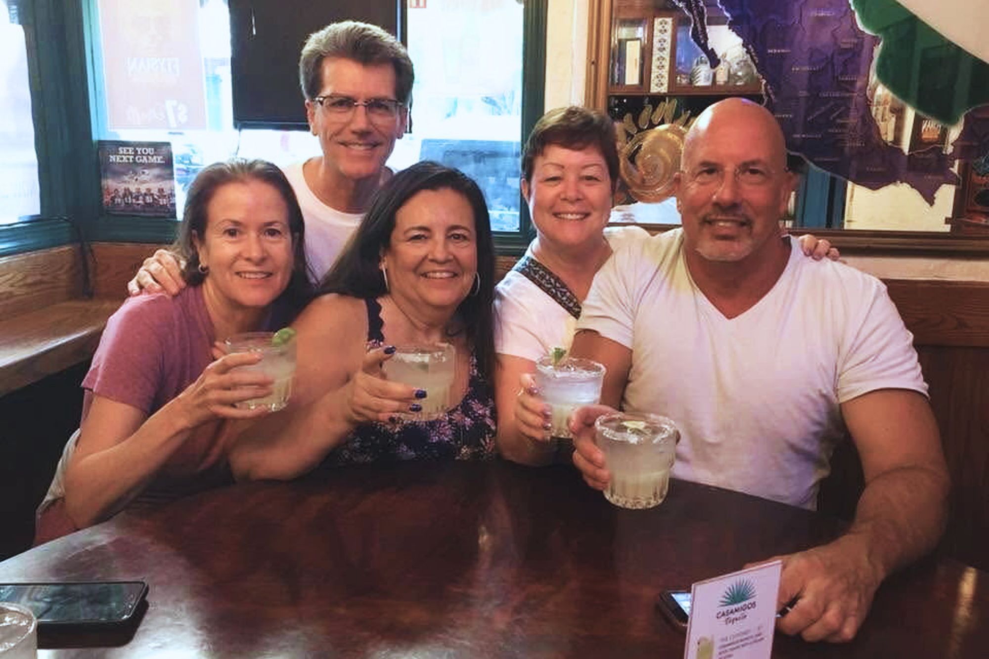 Five friends pose at a bar with drinks in their hands