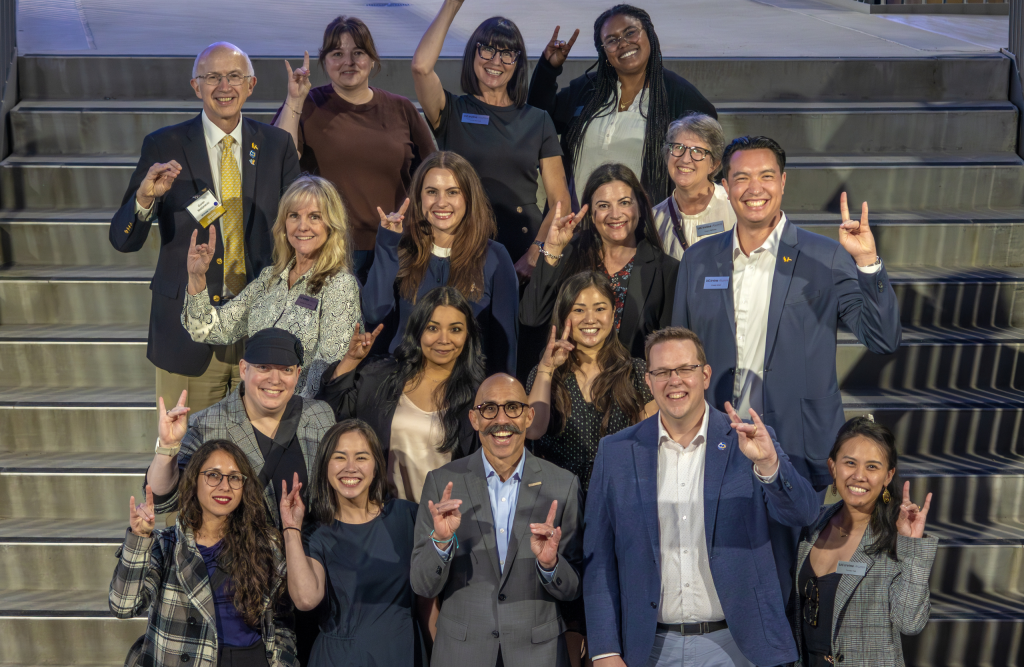 Group of UC Irvine Alumni Staff posing on a staircase at a formal event, making the UC Irvine Anteater hand sign for a group photo.