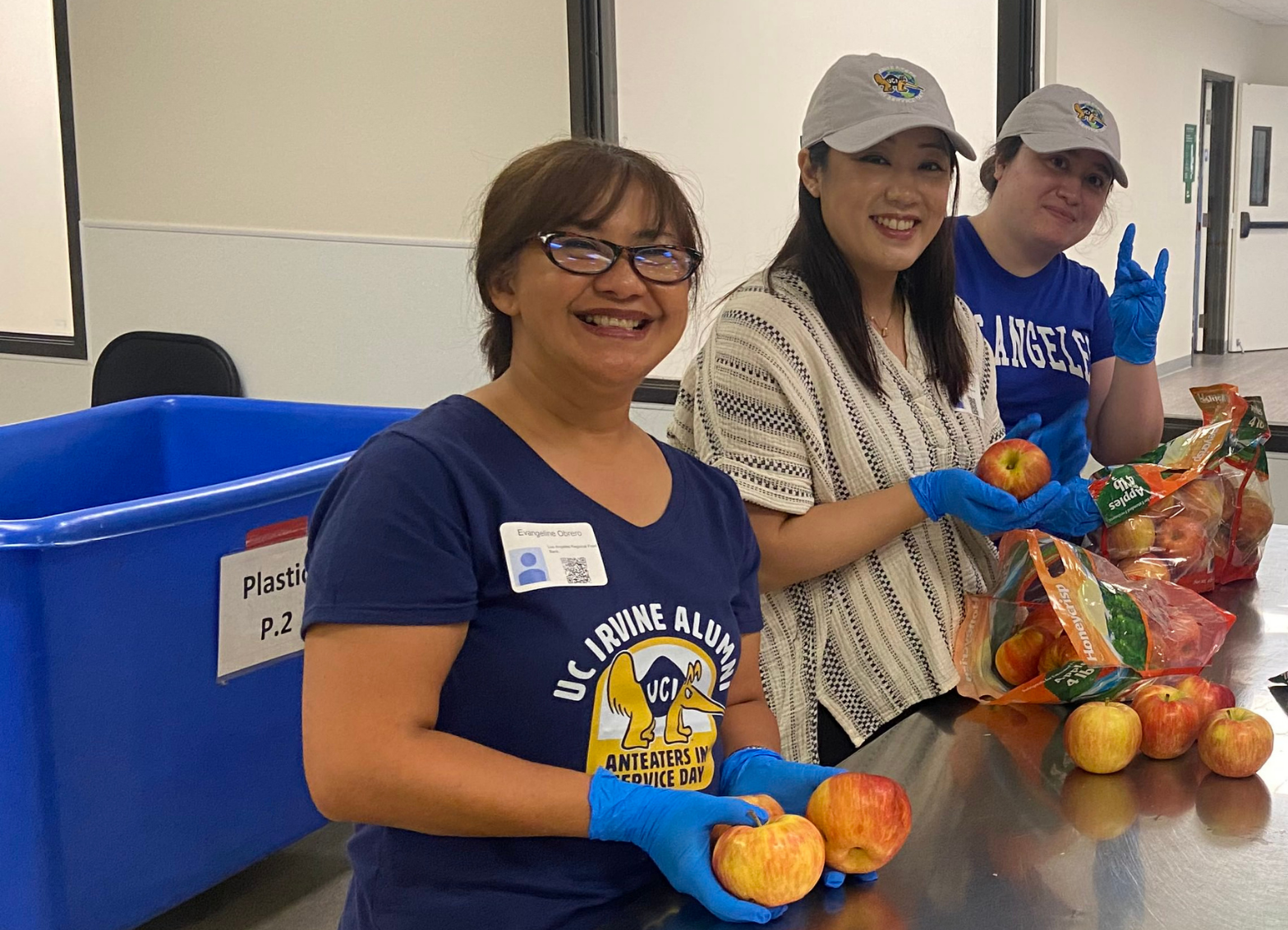 Three volunteers wearing blue gloves sort apples at a food distribution site during the Anteater Service Project Fairfield event.
