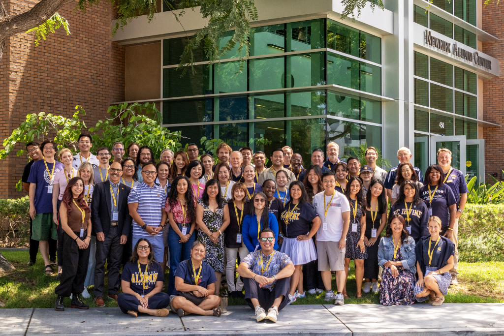 Large group of UC Irvine alumni and volunteers gathered outdoors in front of the Newman Alumni Center for a group photo.