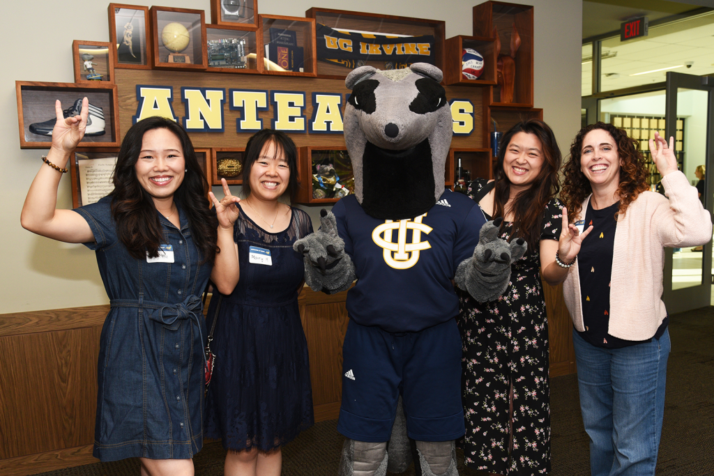 A group of attendees poses with the UC Irvine Anteater mascot in front of an “Anteaters” display, making the school hand sign.