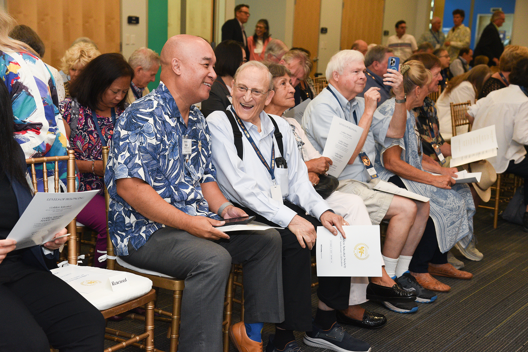 Attendees seated in rows chat and review event programs before a Golden Anteater Society celebration program begins.