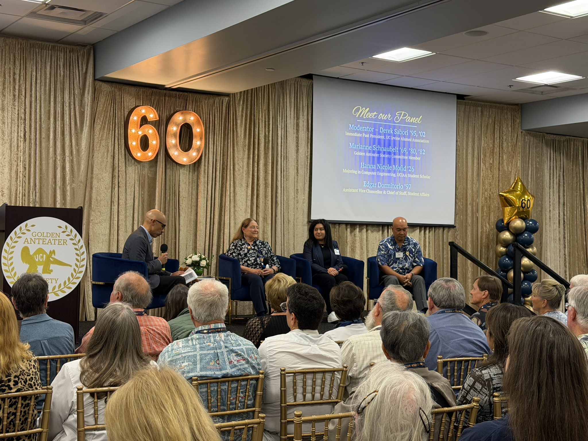 Panelists and a moderator speak during a Golden Anteater Society anniversary celebration as attendees listen from the audience.