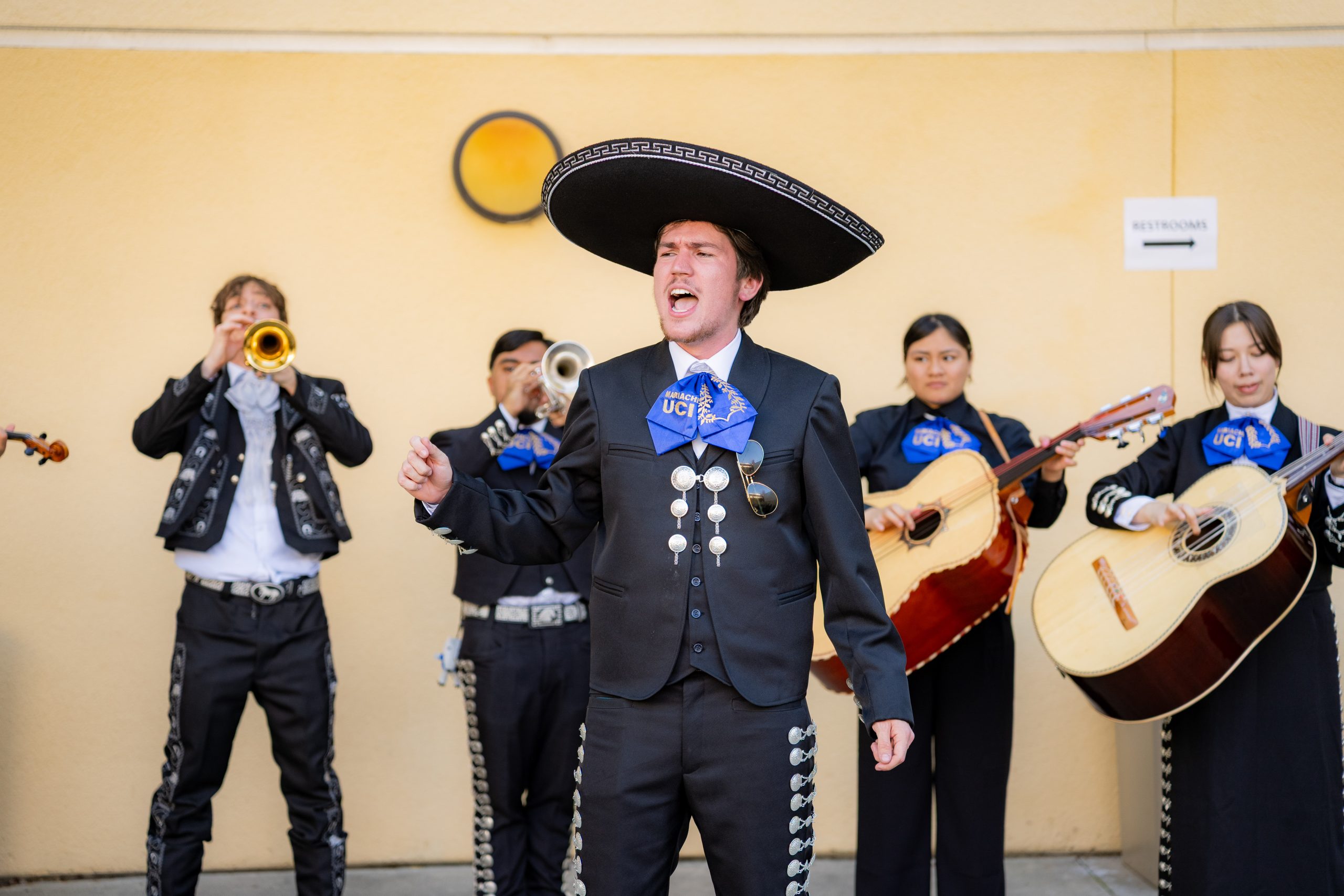 A mariachi ensemble performs during UC Irvine Homecoming, with musicians playing brass and string instruments while a vocalist sings at center stage.