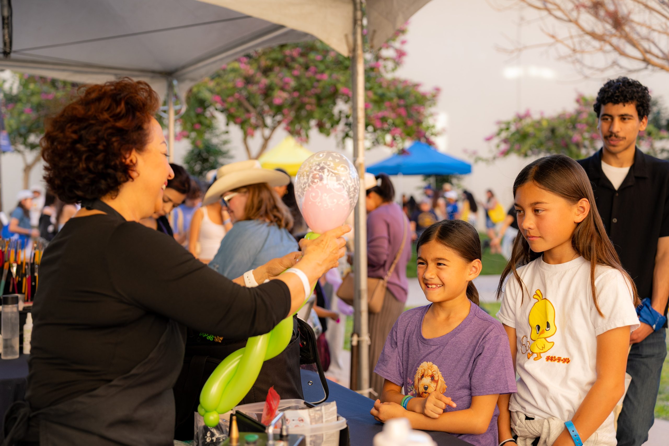 A balloon artist creates a decorative balloon for two children at an activity booth during a UC Irvine Homecoming celebration.