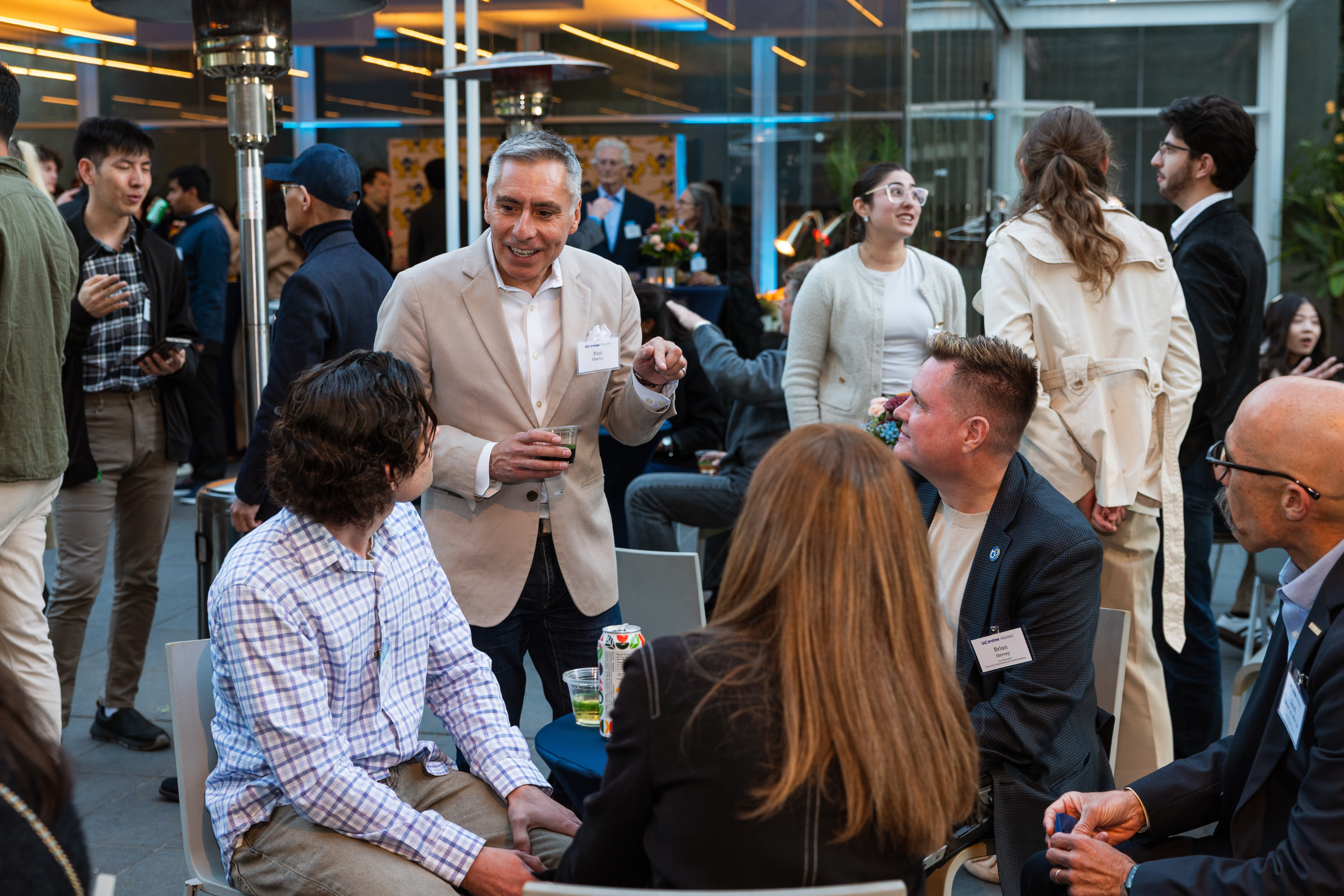 Attendees mingle and converse at an indoor networking event with tables, refreshments, and gathering spaces.