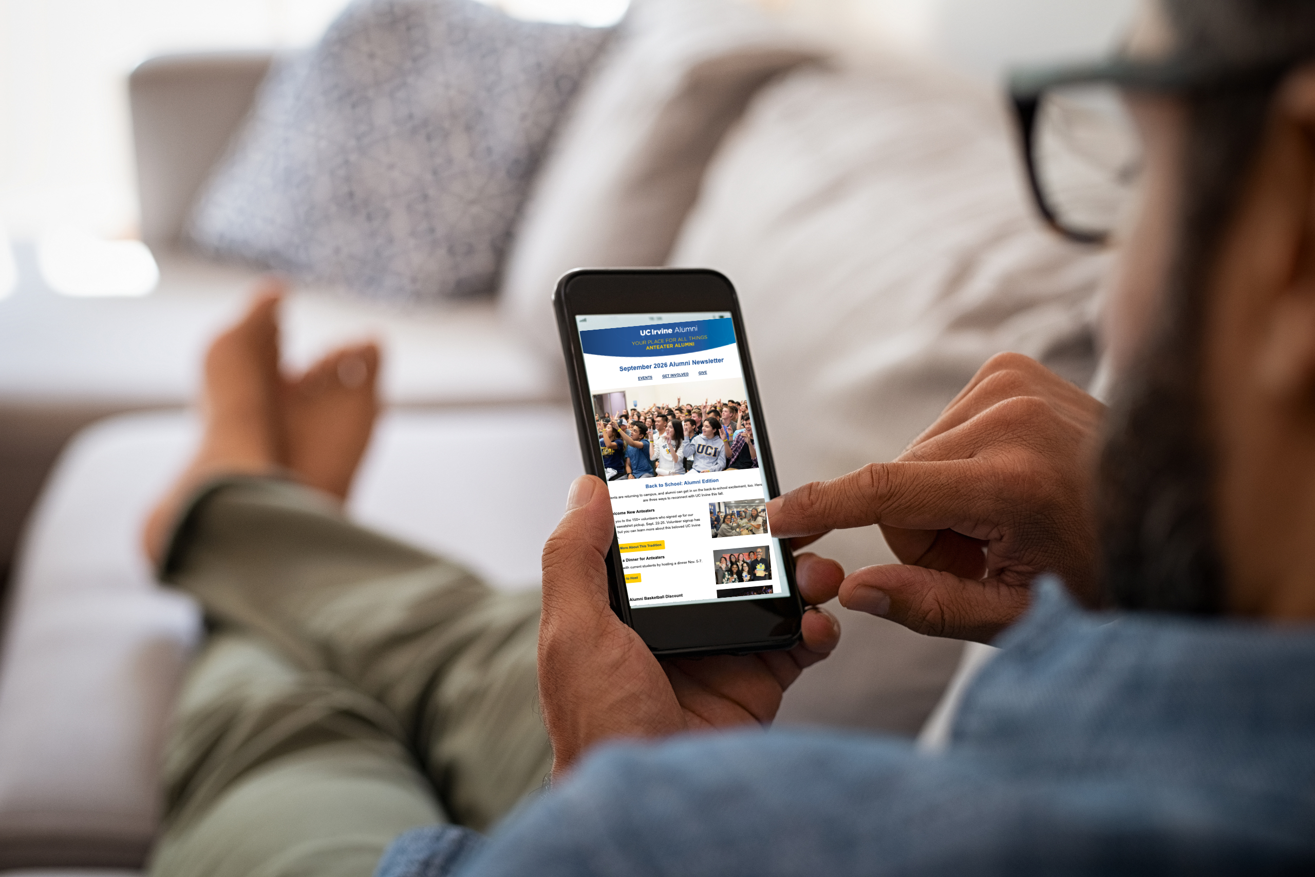 Person viewing the UC Irvine Alumni newsletter on a smartphone while relaxing at home.