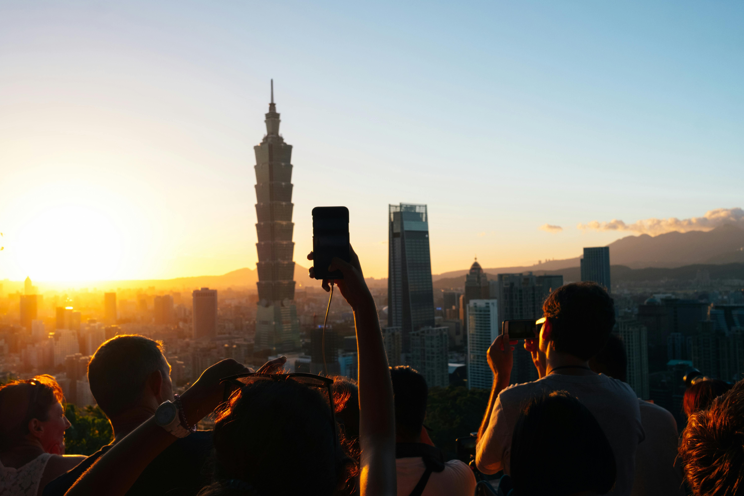 Visitors photograph the Taipei skyline at sunset, with Taipei 101 rising above the city.